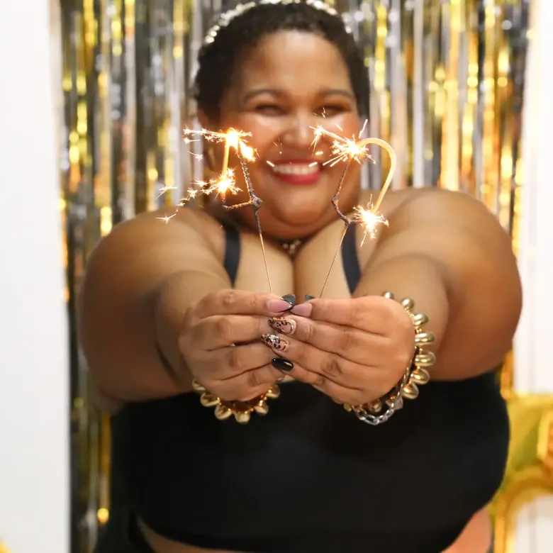 Milestone birthday glam portrait, sparkler held in cupped hands against a gold fringe backdrop