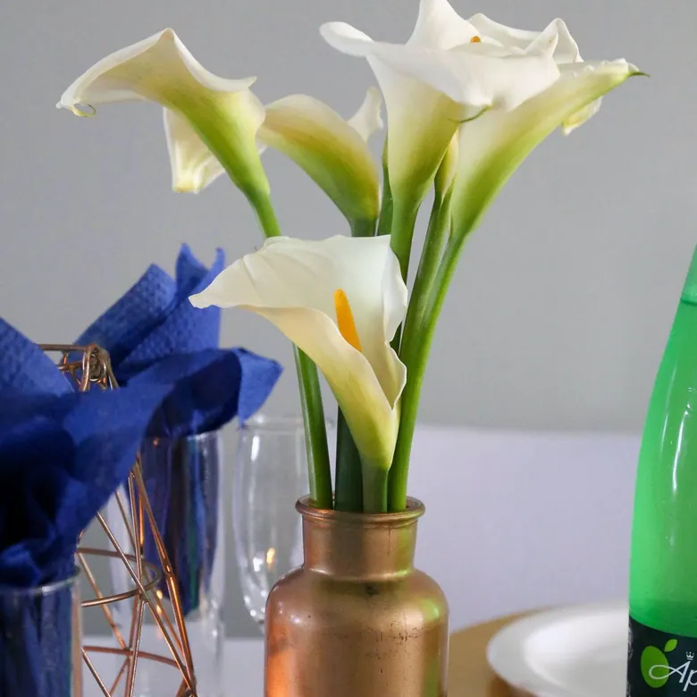 Event styling detail, white calla lilies in a copper vase on a navy and white table setting