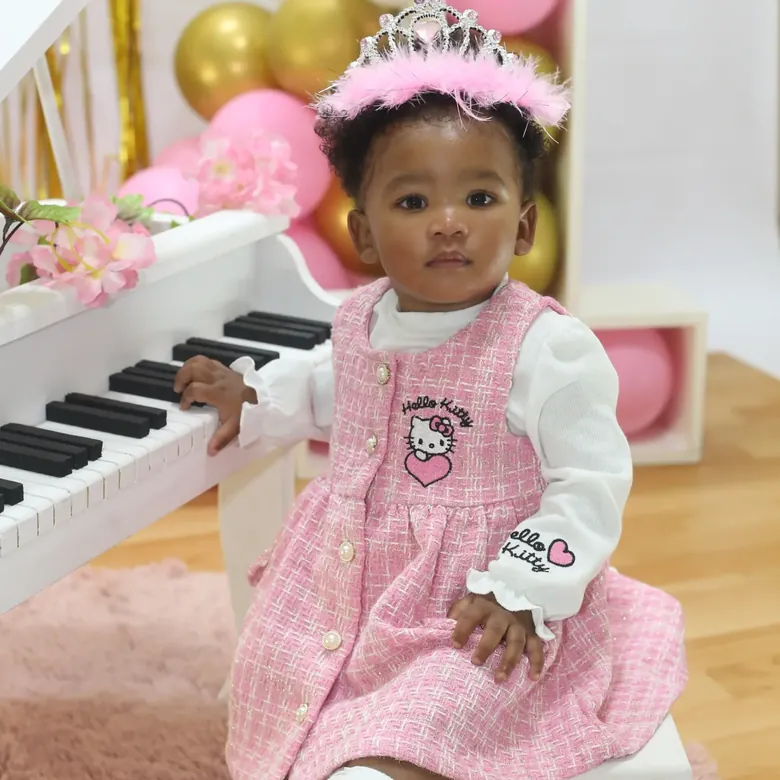 First birthday session, a baby girl in a pink pinafore at a white toy piano