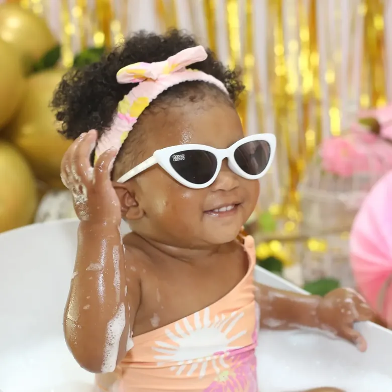 First birthday milk-bath session, a baby girl in white sunglasses sitting in the tub