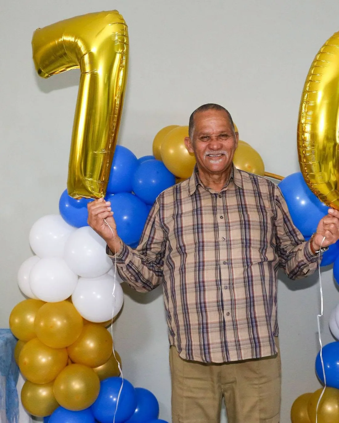 70th birthday celebration, guest of honour holding gold number-seventy balloons in front of a blue and gold balloon arch