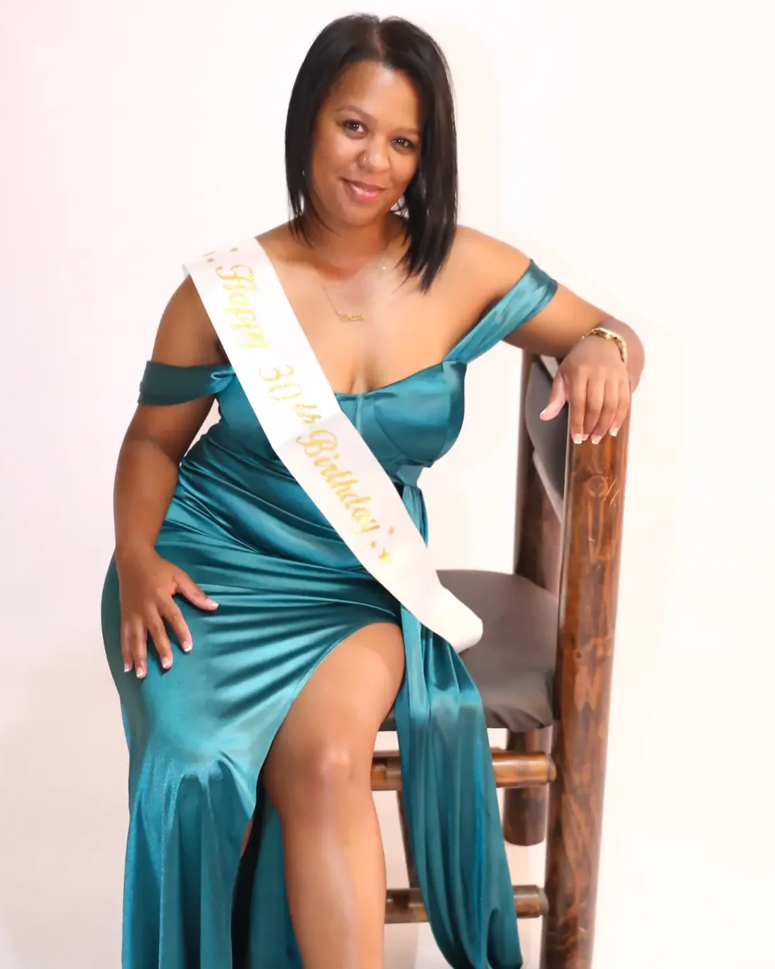 Milestone birthday studio shoot, client in an emerald satin gown seated on a wooden chair with a 30th birthday sash