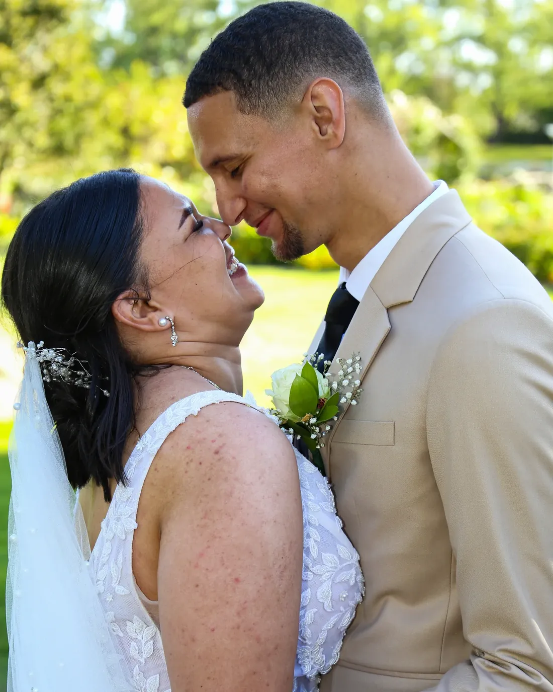 Wedding day portrait, bride in a white gown and veil forehead to forehead with the groom in a beige suit